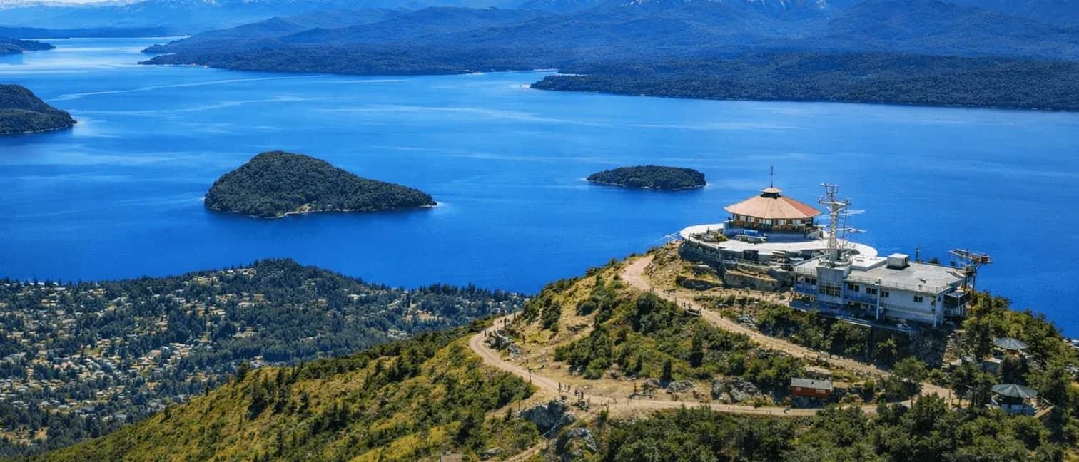 Vista panorámica desde la cumbre del Cerro Otto con la confitería giratoria y el lago Nahuel Huapi rodeado de montañas y bosques, Bariloche.