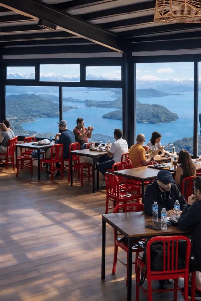 Patio de comidas con personas comiendo y admirando el paisaje panoramico del lago Nahuel Huapi