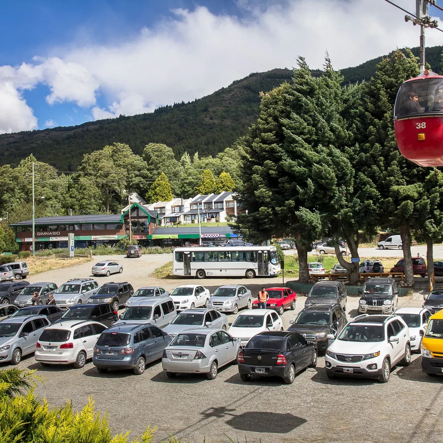 Estacionamiento de la base del Teleférico Cerro Otto con un teleférico ascendiendo y autos debajo