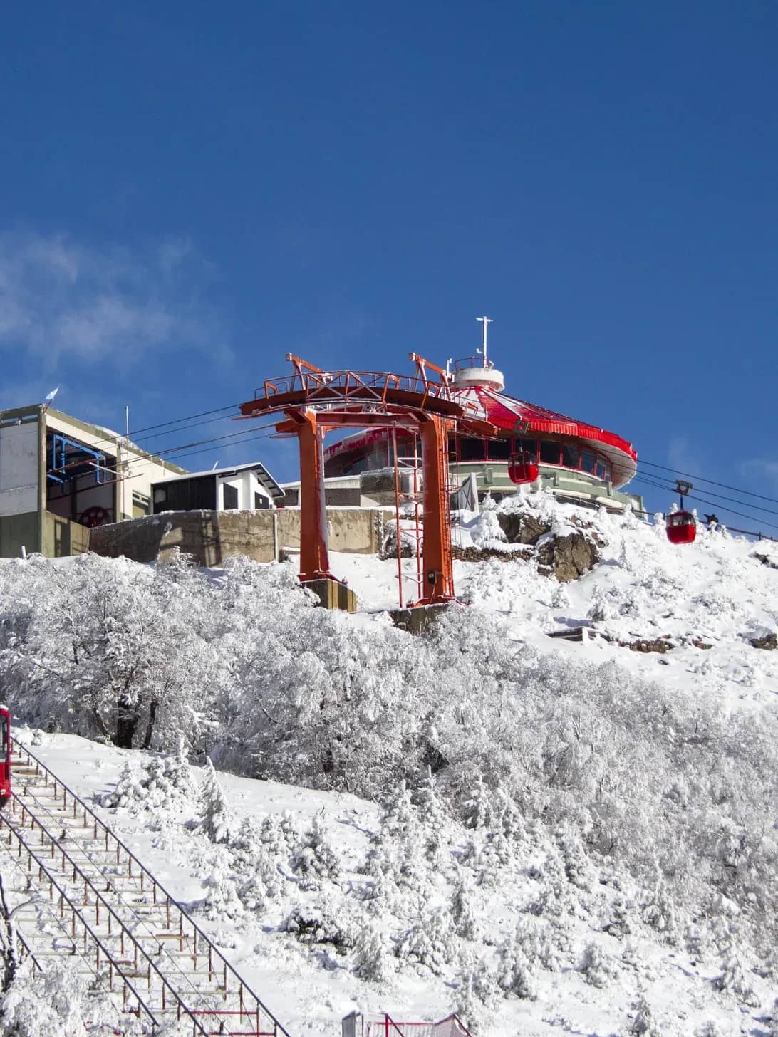 Imagen panorámica de la cumbre del cerro otto nevada donde se aprecian la confiteria giratoria, la estacion superior de los teleféricos y el funicular de la cumbre