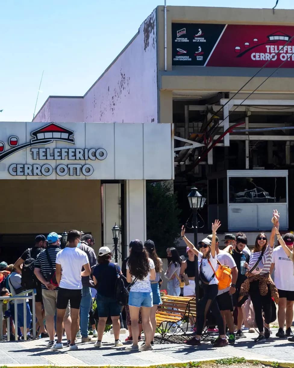 Turistas ingresando por la rampa de entrada a la base con un teleférico despegando.