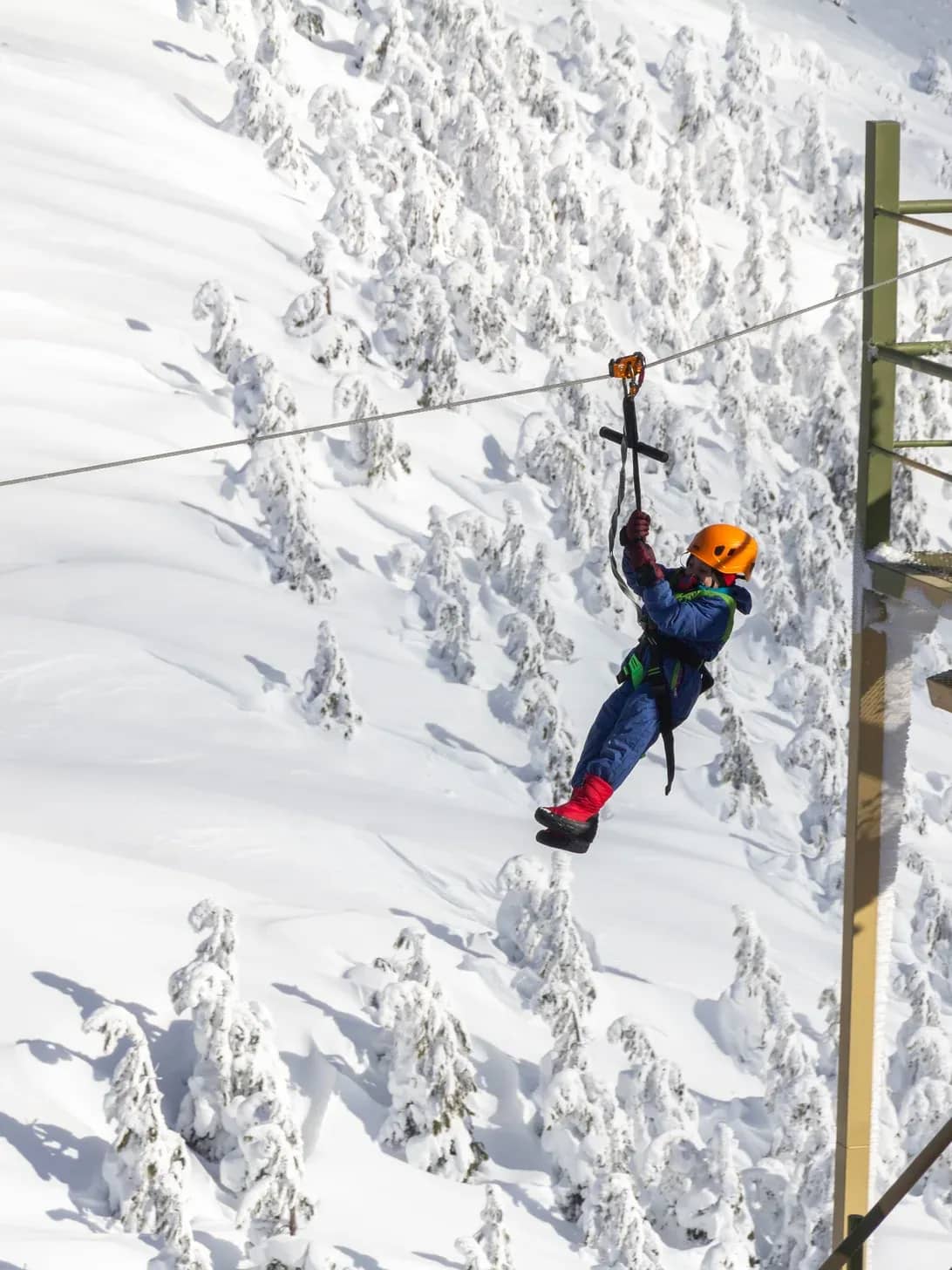 Niña con casco naranja lanzadose desde la tirolesa con un fondo de una montaña nevada